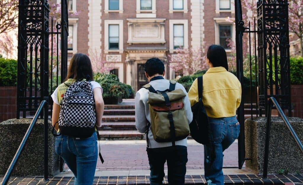 A group of three students walking up stairs to enter their college campus